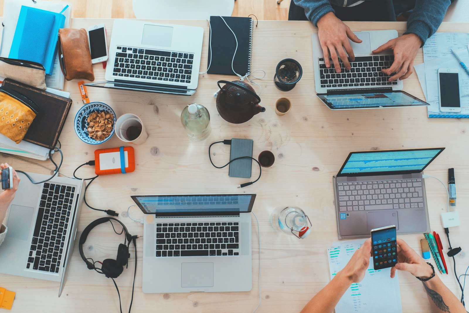Overhead view of a shared desk covered with laptops, notebooks and coffee